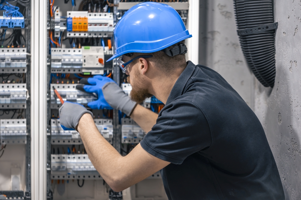 A male electrician works in a switchboard with an electrical connecting cable.